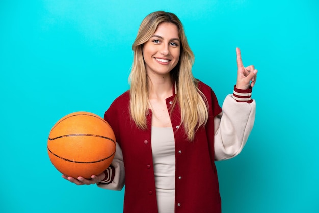 Joven jugadora de baloncesto caucásica aislada de fondo azul mostrando y levantando un dedo en señal de lo mejor