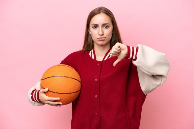 Joven jugadora de baloncesto caucásica sobre fondo rosa aislada mostrando el pulgar hacia abajo con expresión negativa
