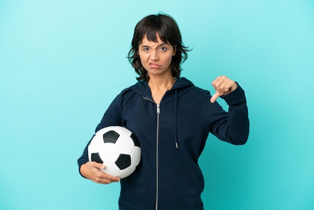 Joven jugadora de fútbol de raza mixta aislada de fondo azul mostrando el pulgar hacia abajo con expresión negativa