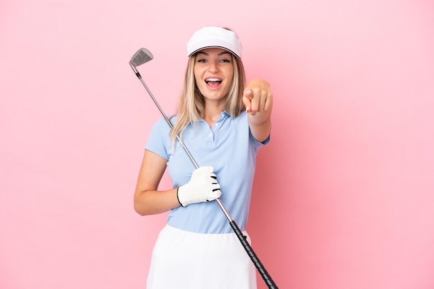 Joven jugadora de golf mujer aislada de fondo rosa sorprendida y apuntando al frente