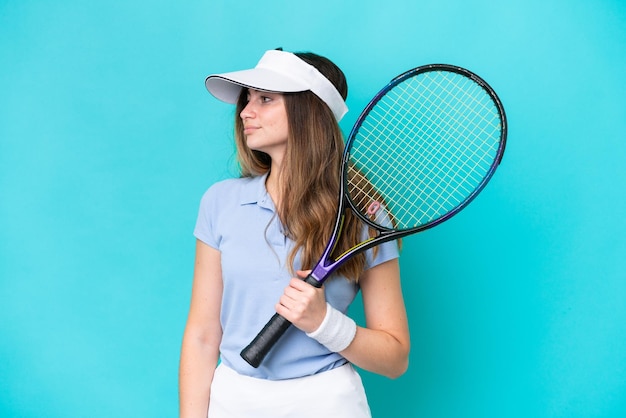 Joven jugadora de tenis aislada en fondo azul mirando hacia el lado