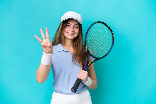 Joven jugadora de tenis mujer aislada en fondo azul feliz y contando tres con los dedos