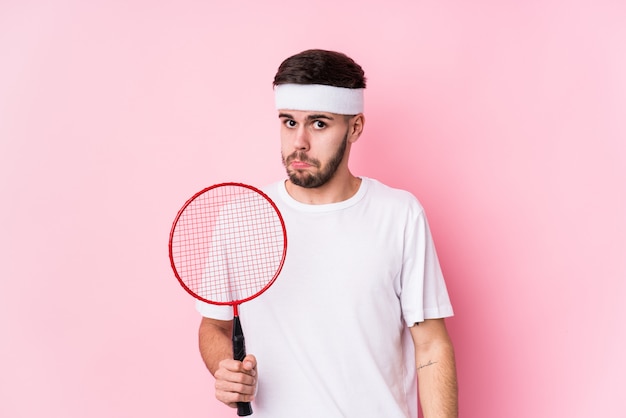 Joven jugando bádminton aislado se encoge de hombros y abre los ojos confundidos