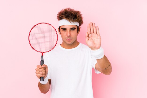 Joven jugando bádminton aislado de pie con la mano extendida mostrando la señal de stop, impidiéndote.