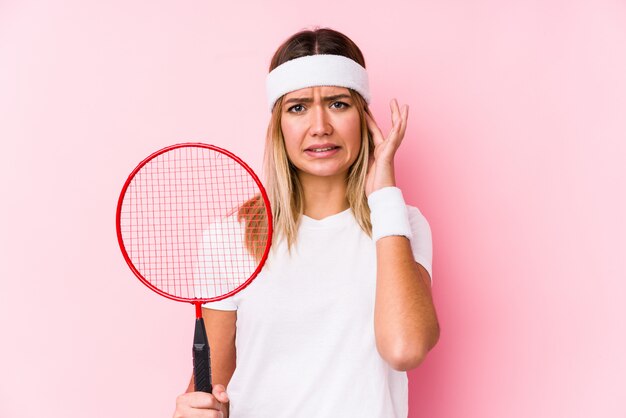 Joven jugando bádminton cubriendo las orejas con las manos.