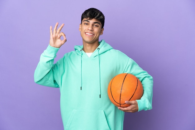 Joven jugando baloncesto en púrpura aislado mostrando signo ok con los dedos