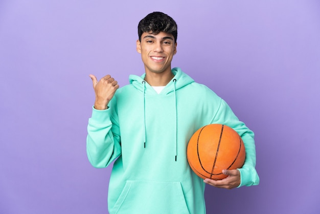 Joven jugando baloncesto sobre fondo púrpura aislado apuntando hacia el lado para presentar un producto