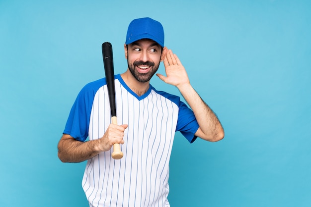 Joven jugando béisbol sobre escuchando algo aislado poniendo la mano en la oreja