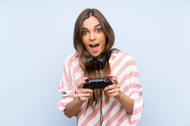 Joven jugando con un controlador de videojuego sobre pared azul aislado