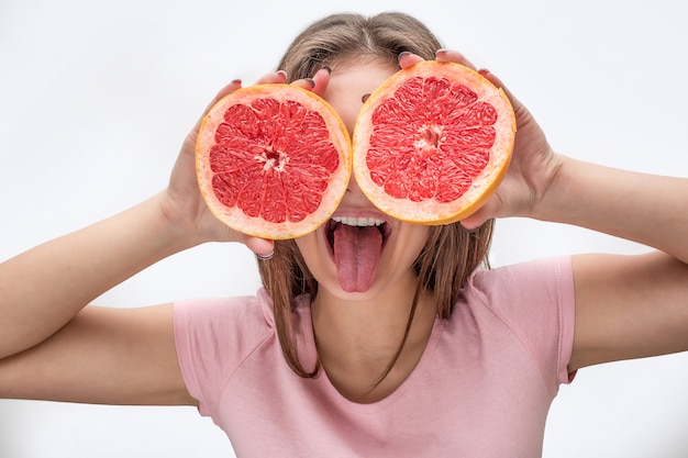 Joven juguetona cubre los ojos con mitades de pomelo