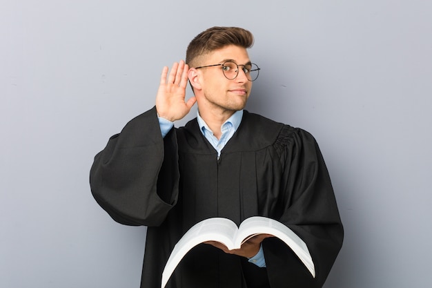 Joven jurista sosteniendo un libro tratando de escuchar un chisme.