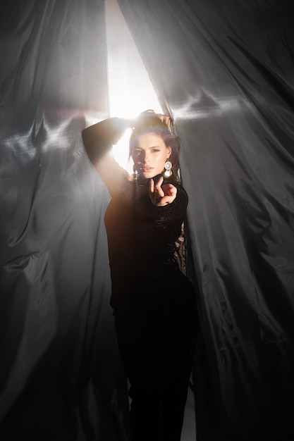 Una joven lánguida con un elegante vestido largo se inclina contra una cortina negra en el estudio