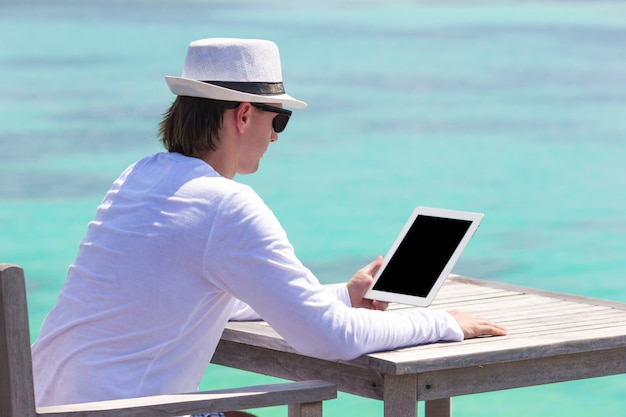 Joven con laptop en playa tropical