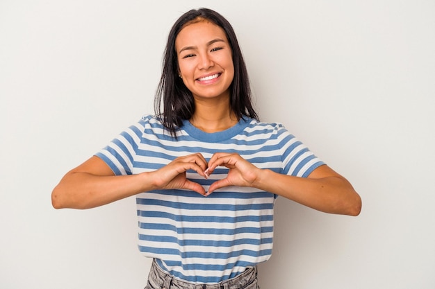 Joven latina aislada de fondo blanco sonriendo y mostrando una forma de corazón con las manos