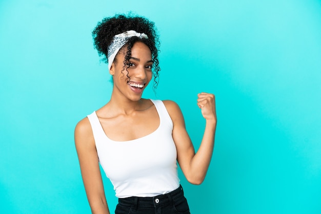 Joven latina aislada sobre fondo azul celebrando una victoria