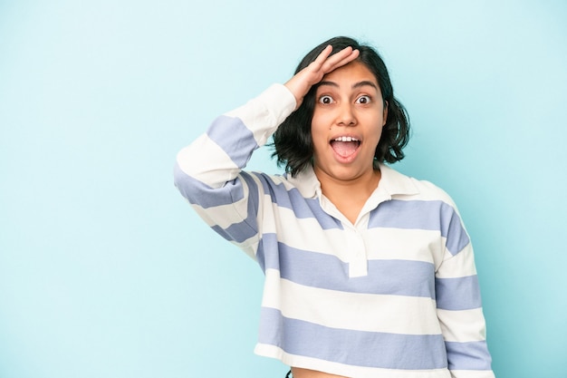 Joven latina aislada sobre fondo azul grita fuerte, mantiene los ojos abiertos y las manos tensas.