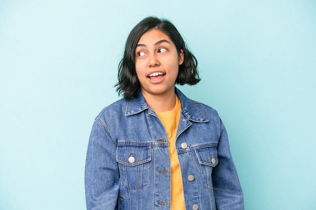 Joven latina aislada sobre fondo azul se ve a un lado sonriente, alegre y agradable.