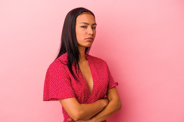 Joven latina aislada sobre fondo rosa sospechoso, incierto, examinándote.