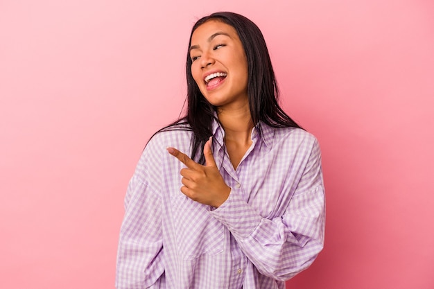 Joven latina aislada sobre fondo rosa se ve a un lado sonriente, alegre y agradable.