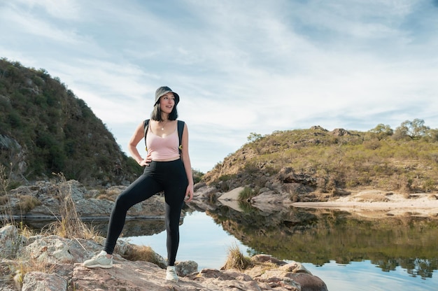 joven latina caminando de pie en una roca en un lago en el medio de dos montañas