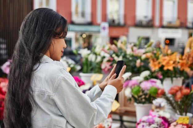 Joven latina capturando la vibrante belleza de las flores en el puesto de un vendedor ambulante