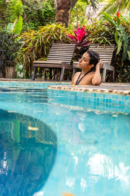 Una joven latina contemplando sentada junto a una piscina natural turquesa