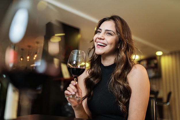 Joven latina con una copa de vino tinto en la barra.