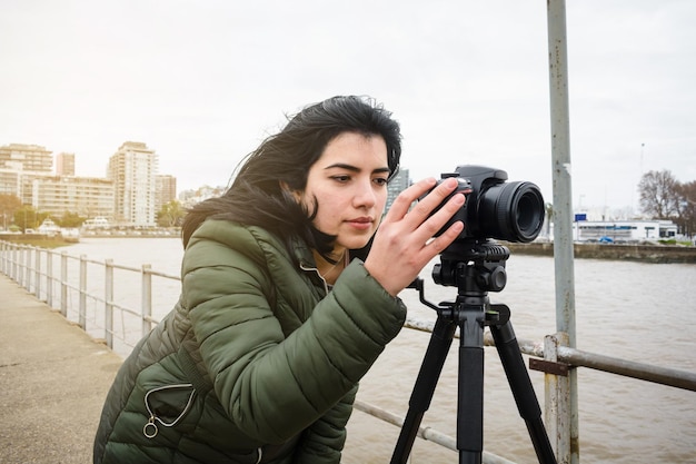 Foto joven latina creadora de contenido en el muelle revisando el video que hizo con su cámara digital