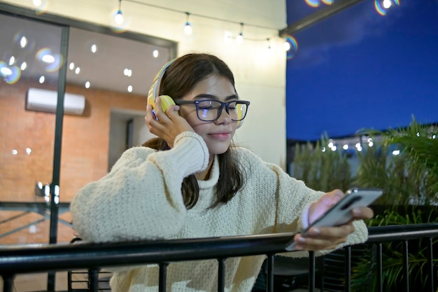 Joven latina envía mensajes desde su celular mientras escucha música en un paisaje nocturno