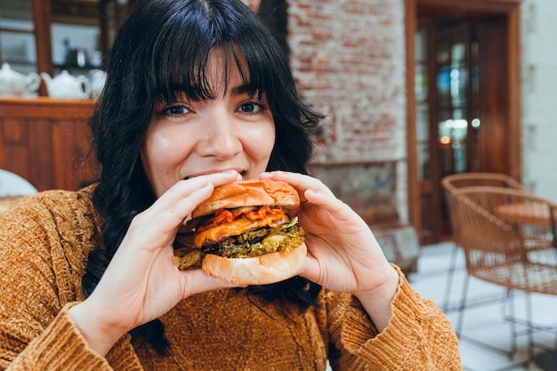 joven latina feliz comiendo hamburguesa y mirando a la cámara