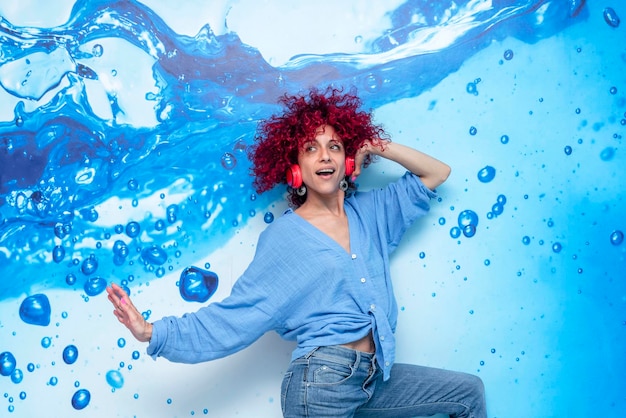 una joven latina feliz con el pelo afro rojo bailando y escuchando música en sus auriculares