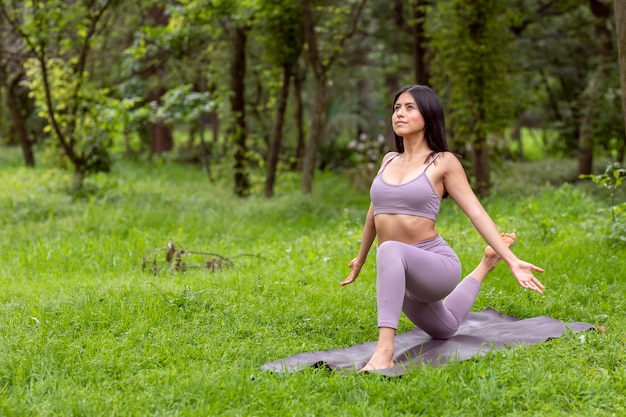 Joven latina haciendo posturas de yoga en el parque al aire libre