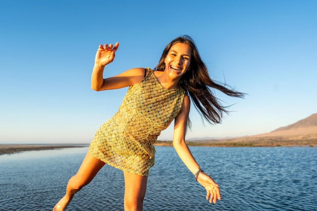 Joven latina jugando feliz en el agua vestida al atardecer