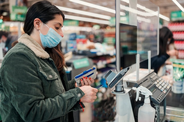 Joven latina pagando con tarjeta en caja registradora en supermercado o negocio