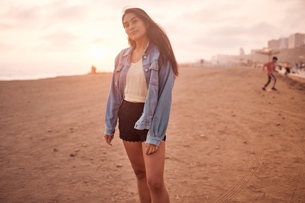 Joven latina posa caminando sobre la arena durante una hermosa puesta de sol