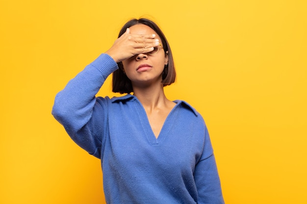 Foto joven latina que cubre los ojos con una mano sintiéndose asustada o ansiosa, preguntándose o esperando ciegamente una sorpresa