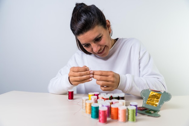 Joven latina que no ve enhebrar una aguja cosiendo ropa hilos coloridos