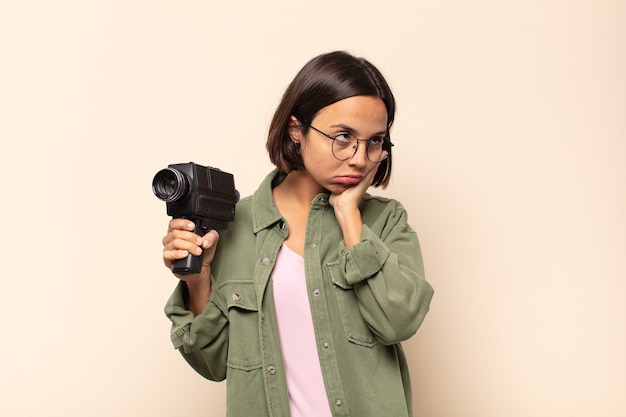 Joven latina que se siente aburrida, frustrada y con sueño después de una tarea tediosa, aburrida y tediosa, sosteniendo la cara con la mano