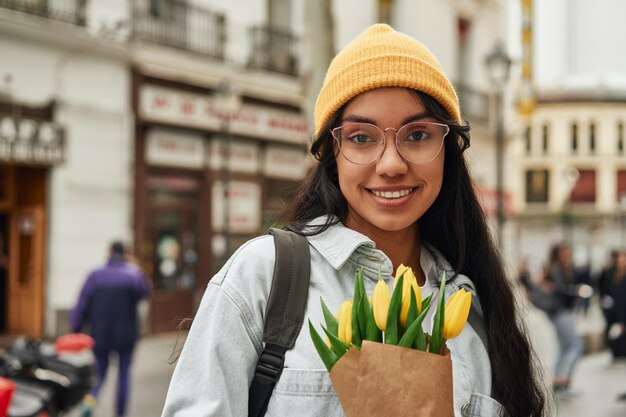 Joven latina radiante con tulipanes soleados en una calle vibrante de la ciudad