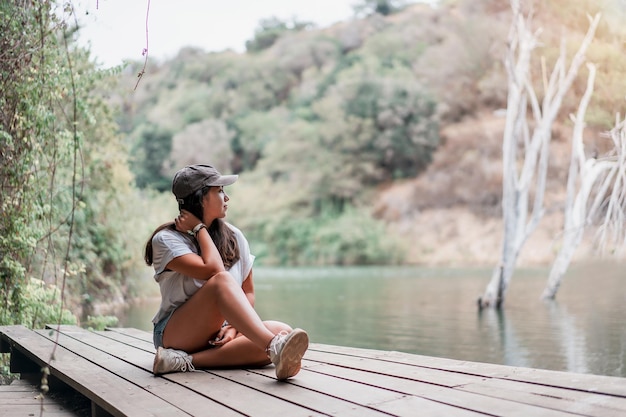 Joven latina sentada en el muelle del lago disfrutando de la vista