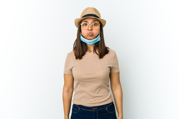 Joven latina con sombrero y máscara para protegerse de los golpes de covid en las mejillas, tiene expresión cansada. Concepto de expresión facial.