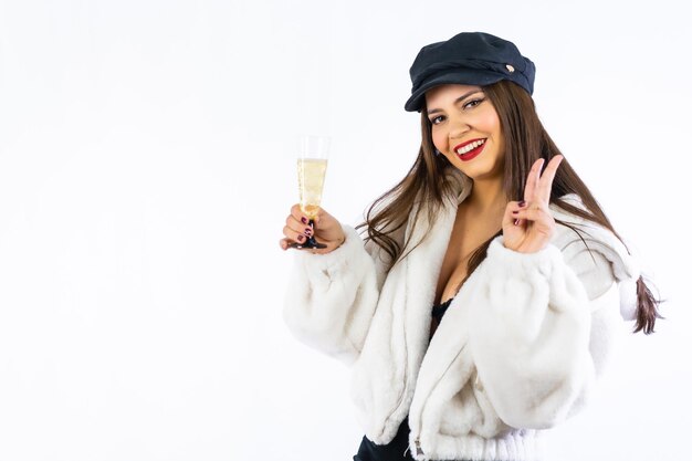 Joven latina con sombrero negro celebrando la víspera de año nuevo sobre un fondo blanco. Con una copa de champagne muy sonriente