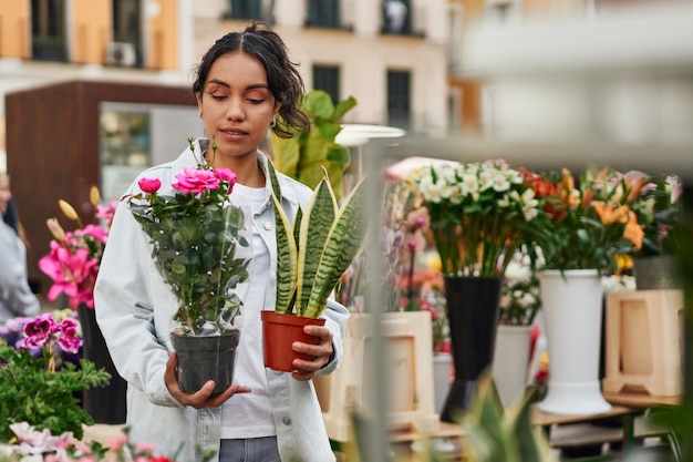 Joven latina sonriendo mientras compra plantas en el puesto de un vendedor ambulante