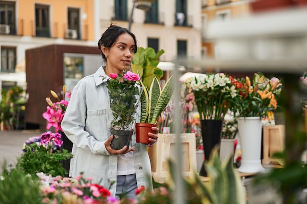 Joven latina sonriendo mientras compra plantas en el puesto de un vendedor ambulante