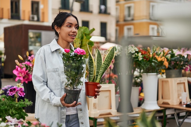 Joven latina sonriendo mientras compra plantas en el puesto de un vendedor ambulante