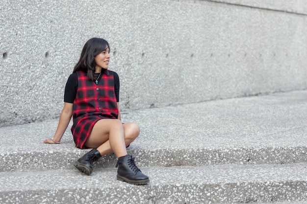 Joven latina sonriendo mientras mira el horizonte sentada en unas escaleras de la ciudad