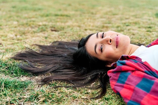 Joven latina sonriente tumbada al aire libre con el pelo en la hierba