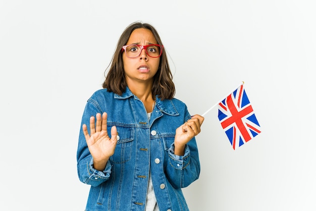 Joven latina sosteniendo una bandera inglesa aislada está conmocionada debido a un peligro inminente