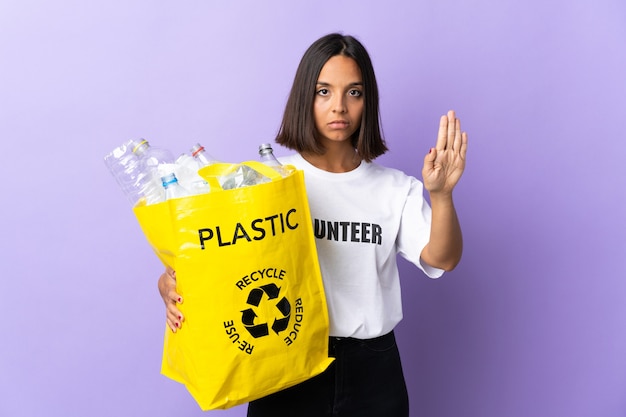 Joven latina sosteniendo una bolsa de reciclaje llena de papel para reciclar