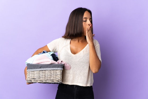 Joven latina sosteniendo una canasta de ropa